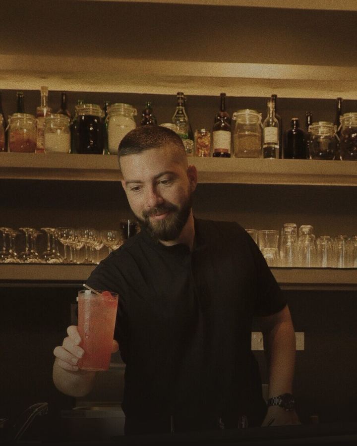 Enzo Ruiz serving a cocktail at the bar of Stillroom, with jars of ferments behind him